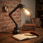 Vintage-style desk lamp on a wooden table with books and an open notebook.