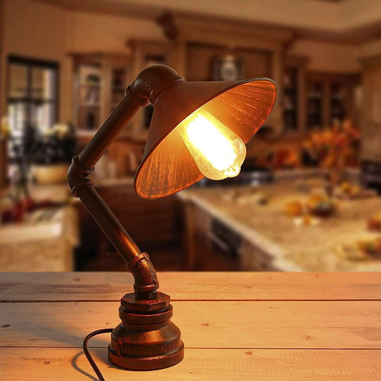 A brown, brushed silver table lamp with an incandescent bulb, featuring a rustic, steampunk-style design, placed on a wooden surface in a home interior setting.