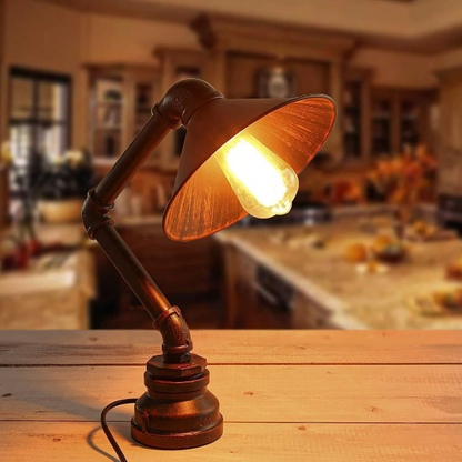 A brown, brushed silver table lamp with an incandescent bulb, featuring a rustic, steampunk-style design, placed on a wooden surface in a home interior setting.